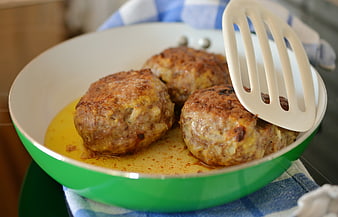 Fried meatballs in a green pan with a white spatula