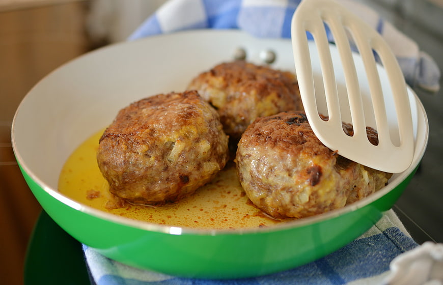 Fried meatballs in a green pan with a white spatula