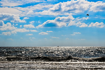 Sparkling ocean waves under blue sky with clouds and parasail