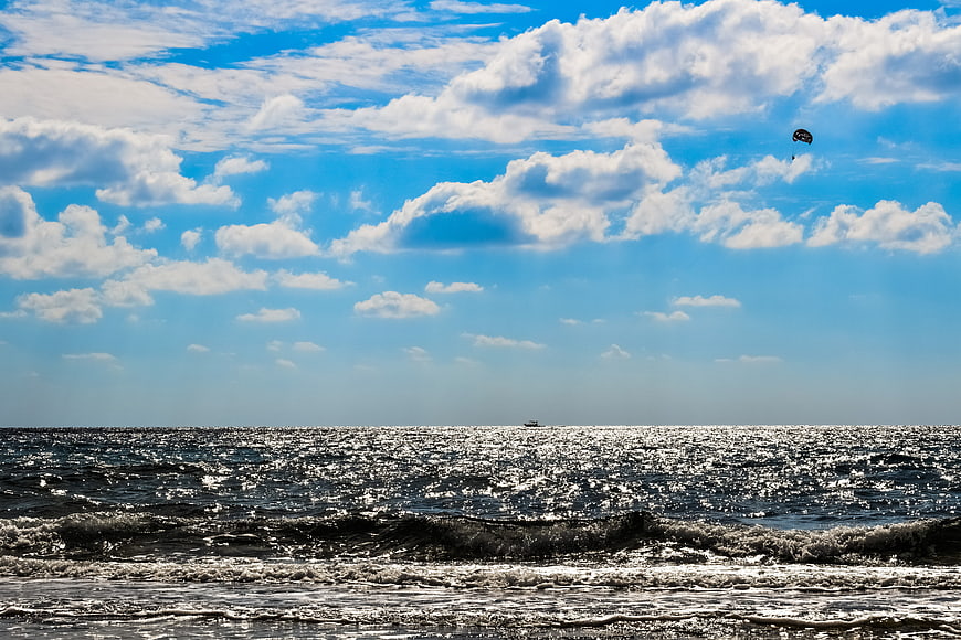 Sparkling ocean waves under blue sky with clouds and parasail