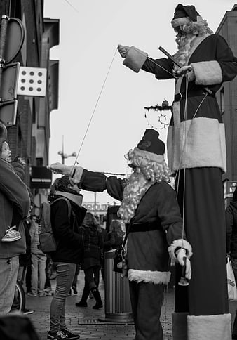 Black and white photo of Santa Claus stilt walkers performing on street