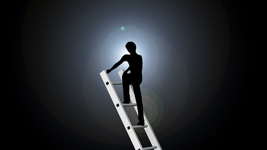 Silhouette of man climbing ladder reaching for light bulb