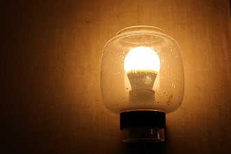Illuminated light bulb inside glass jar with water droplets