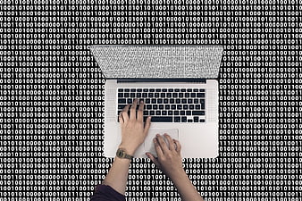 Top view of hands typing on laptop with binary code background