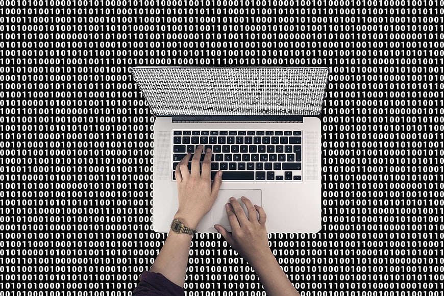 Top view of hands typing on laptop with binary code background