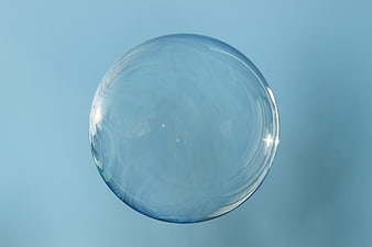 Large Clear Soap Bubble Floating Against Soft Blue Background