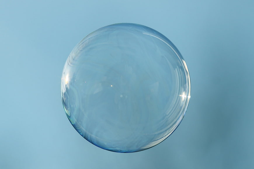Large Clear Soap Bubble Floating Against Soft Blue Background