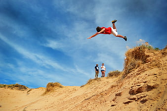 Young man jumping off a sandy cliff into the blue sky