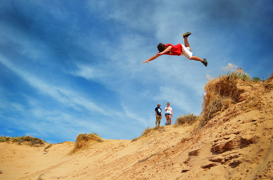 Young man jumping off a sandy cliff into the blue sky