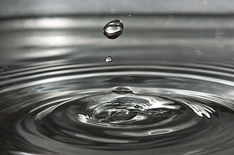 Macro water droplet splash with ripples on dark surface