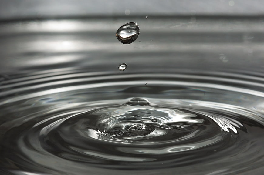 Macro water droplet splash with ripples on dark surface
