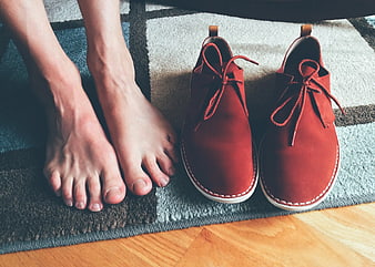 Bare Feet Next to Red Suede Shoes on Rug