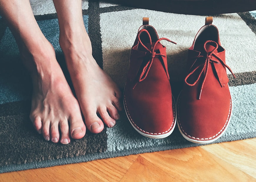 Bare Feet Next to Red Suede Shoes on Rug