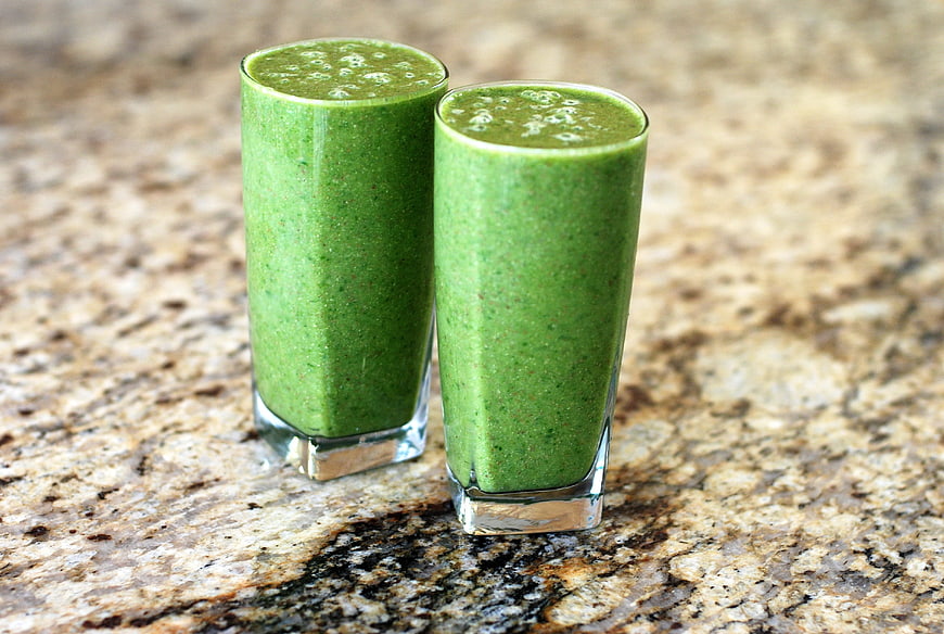 Two glasses of green vegetable smoothie on granite countertop