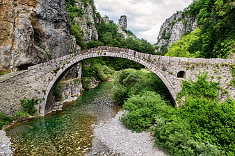 Ancient stone arch bridge over clear river in rocky gorge