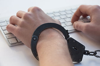 Handcuffed hands typing on computer keyboard symbolizing addiction