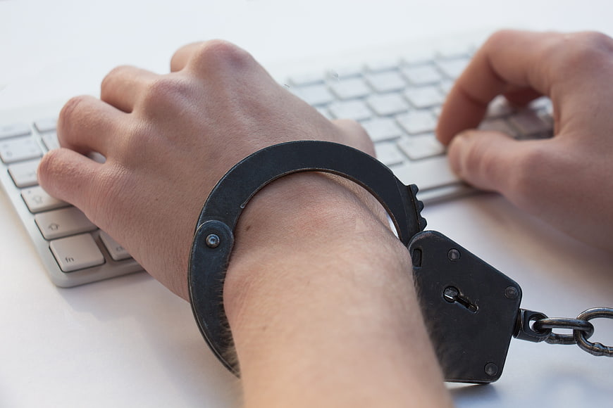 Handcuffed hands typing on computer keyboard symbolizing addiction