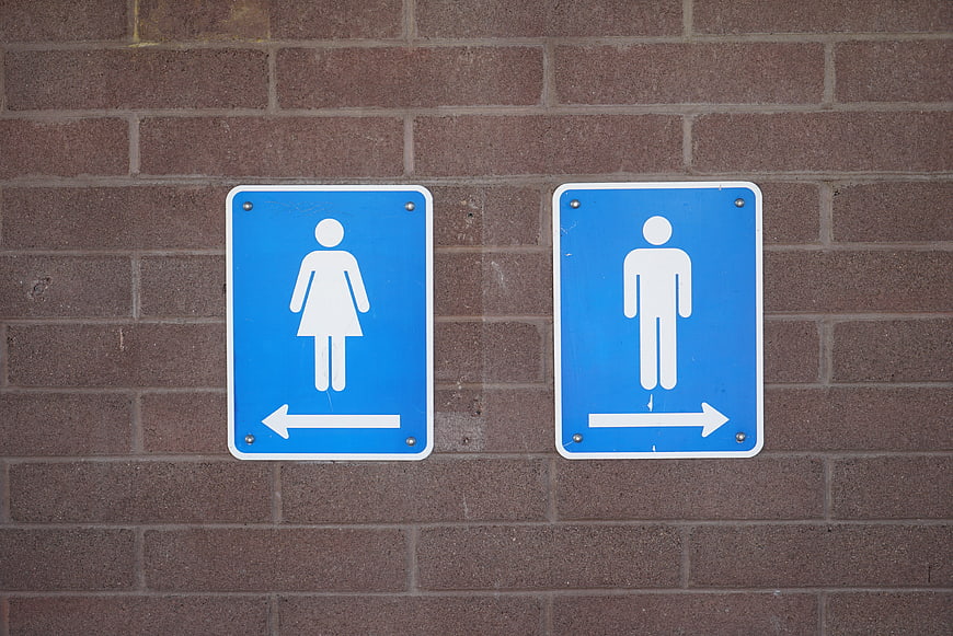 Blue restroom signs with directional arrows on a textured brick wall