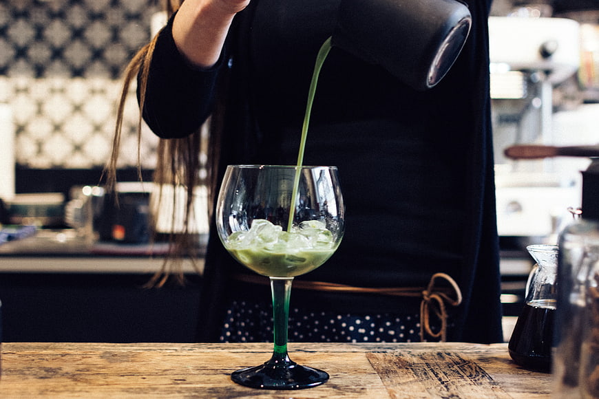 Barista pouring green matcha drink into glass with ice