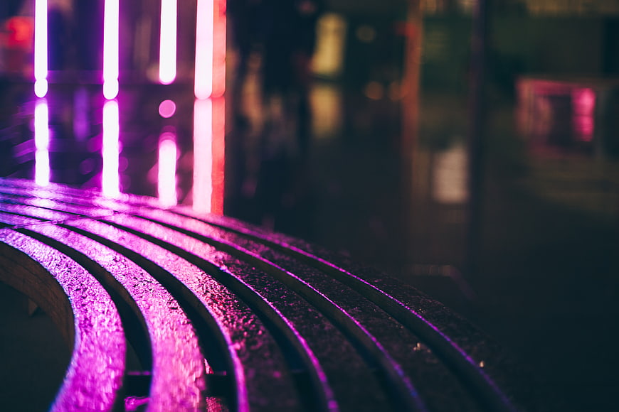 Neon purple lights reflecting on wet curved bench at night