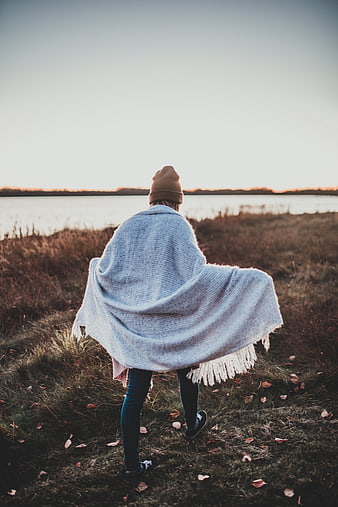 Woman in Knit Poncho Walking by Lake at Sunset
