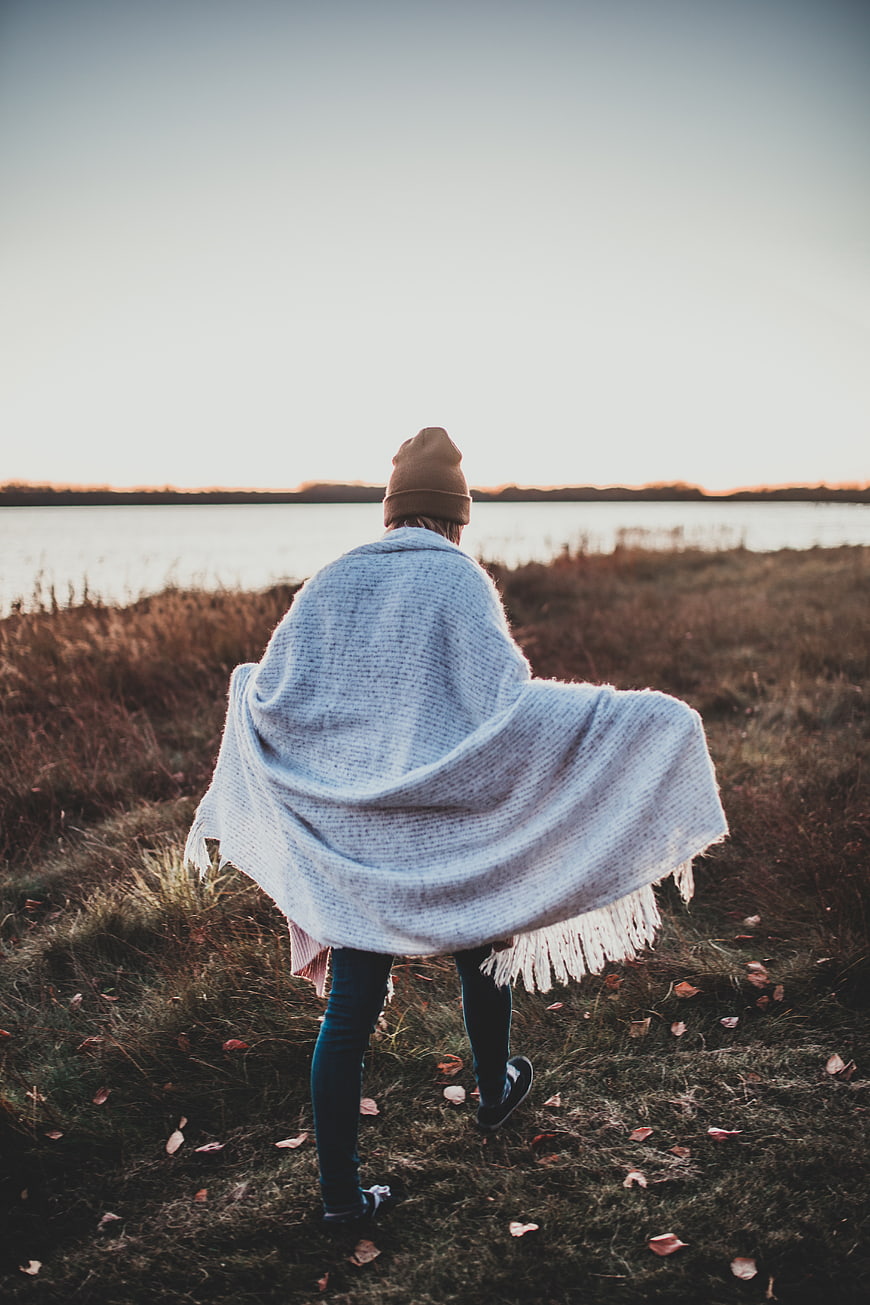 Woman in Knit Poncho Walking by Lake at Sunset