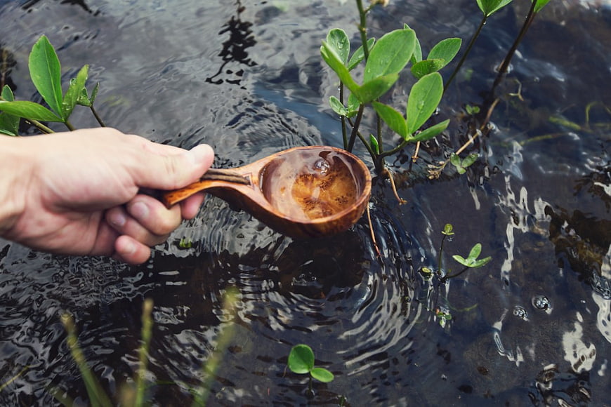 Hand Scooping Water with Wooden Spoon in Stream