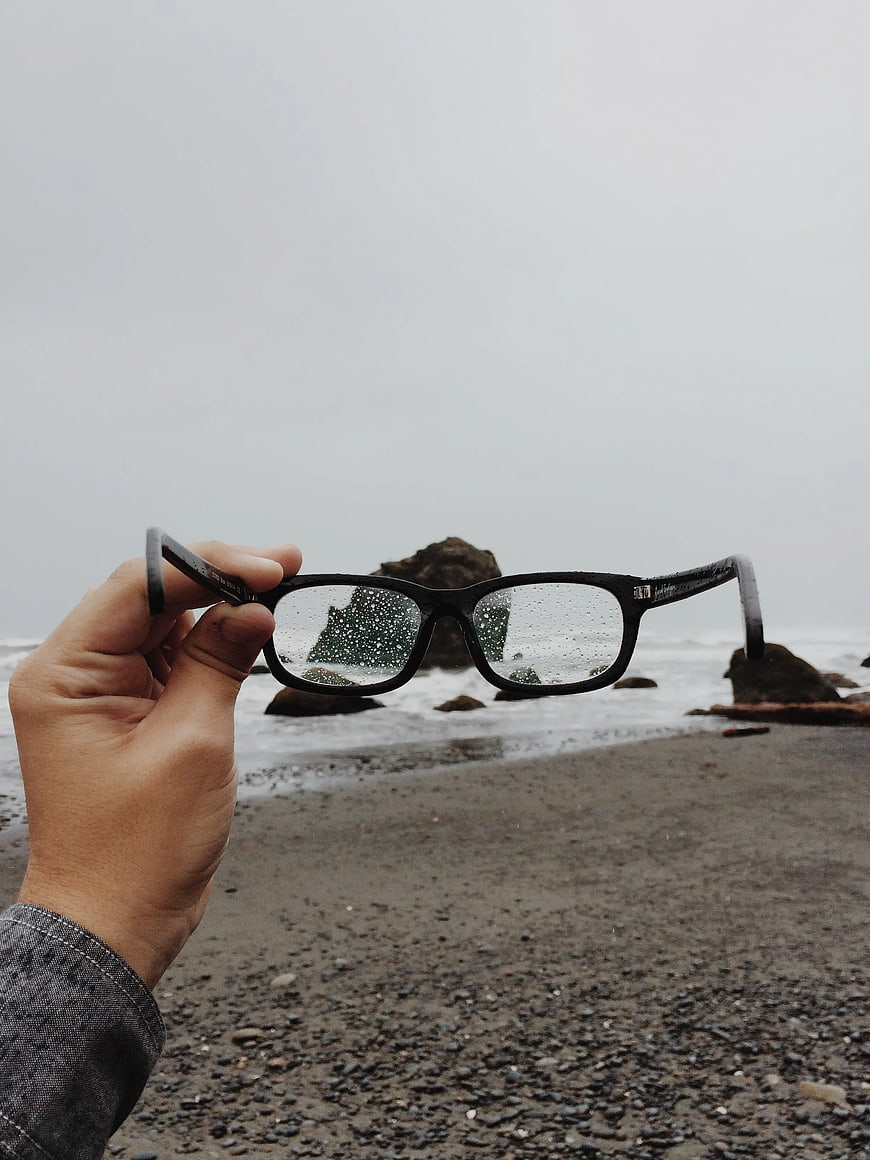 Hand holding rain-speckled glasses on a misty beach