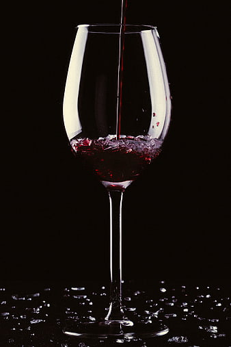 Red wine pouring into glass on black background