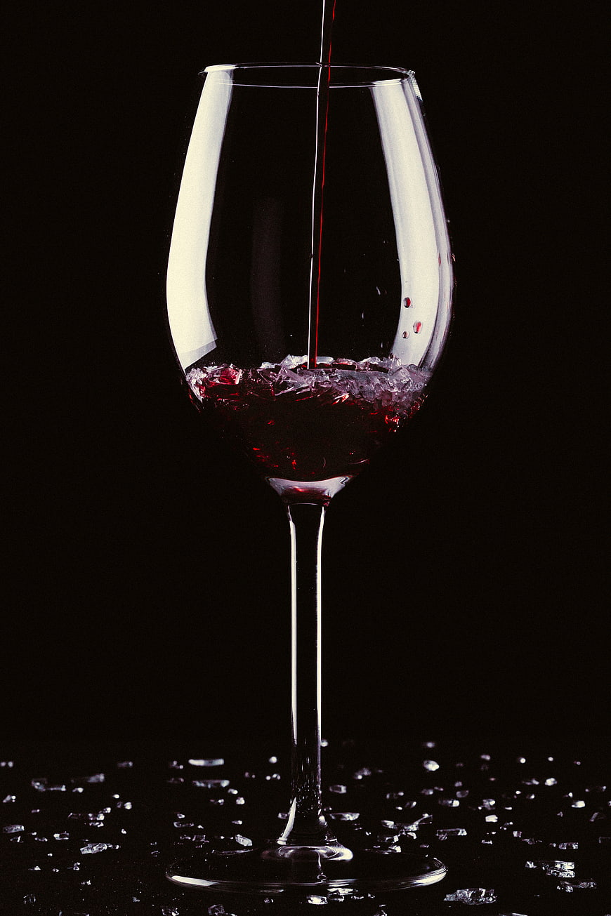Red wine pouring into glass on black background