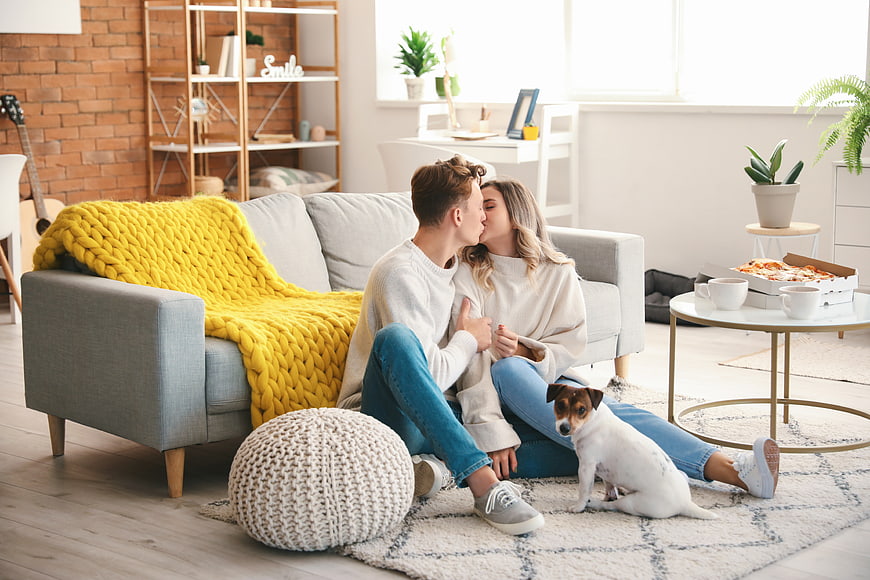 Happy couple kissing on living room floor with dog and pizza