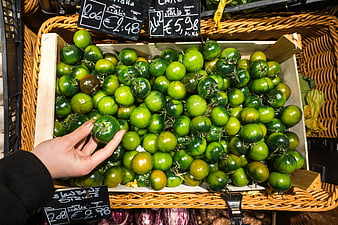 Hand selecting green striped Italian tomatoes at market