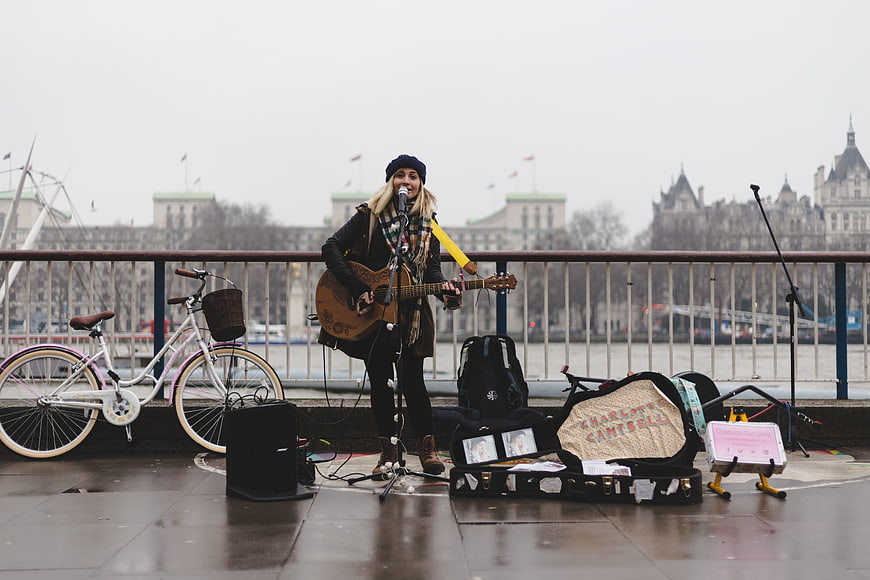 Female busker playing guitar on London bridge