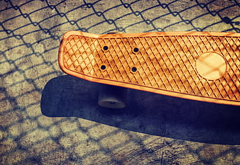 Orange Skateboard on Concrete with Chain Link Shadow