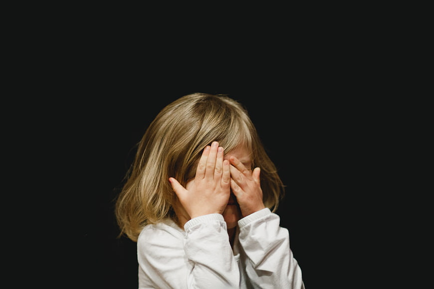 Child covering face with hands against black background