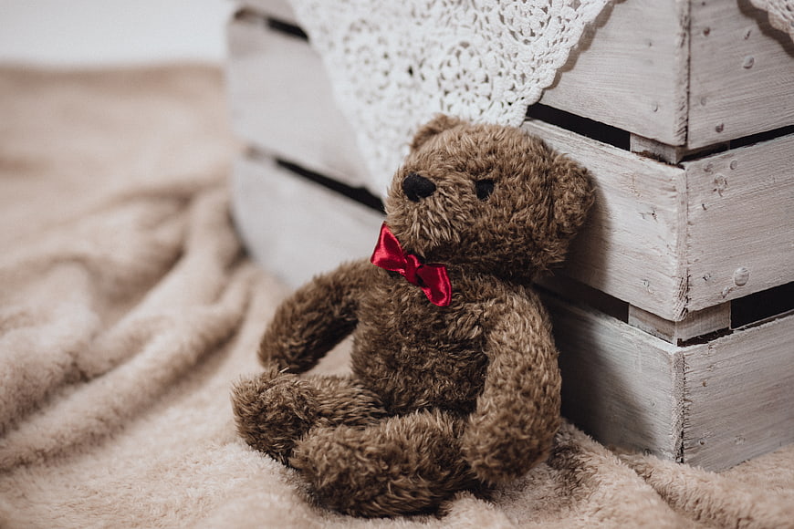 Brown teddy bear with red bow on beige blanket