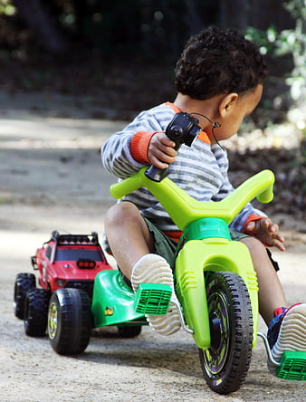 Toddler boy riding green tricycle pulling red toy truck