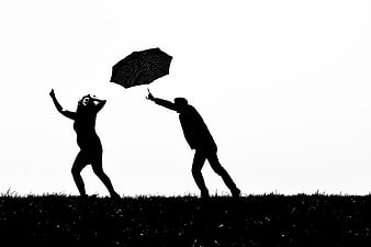Silhouette of pregnant couple playing with umbrella in rain