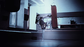 Female Muay Thai Fighter Kicking Punching Bag in Gym