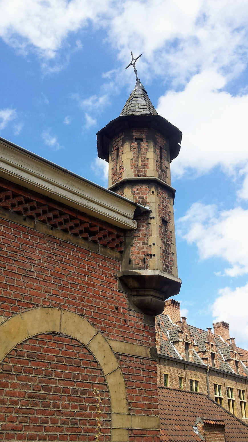 Low angle view of historic brick church tower with cross against blue sky