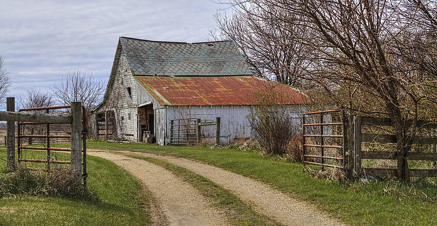 Rustic Old Farmhouse With Gravel Path And Rusty Metal Gates