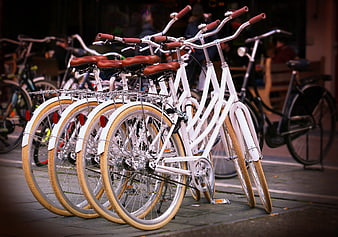 Row of white city bicycles with brown seats parked on sidewalk