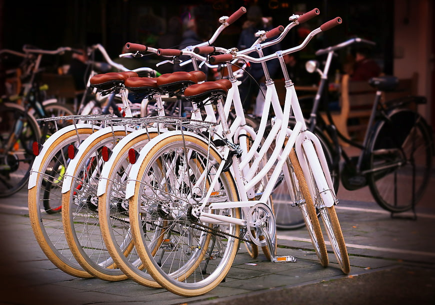 Row of white city bicycles with brown seats parked on sidewalk
