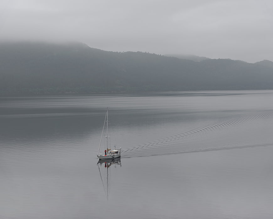 Lone Sailboat on Misty Lake with Mountain Background