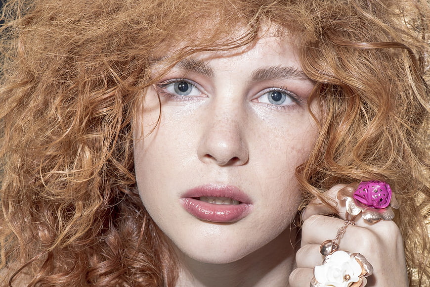 Close-up portrait of a young woman with curly red hair and floral jewelry