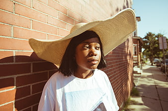 Stylish Black Woman in Wide Brim Hat Against Brick Wall