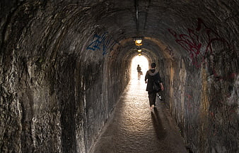 Woman walking through dark stone tunnel towards light