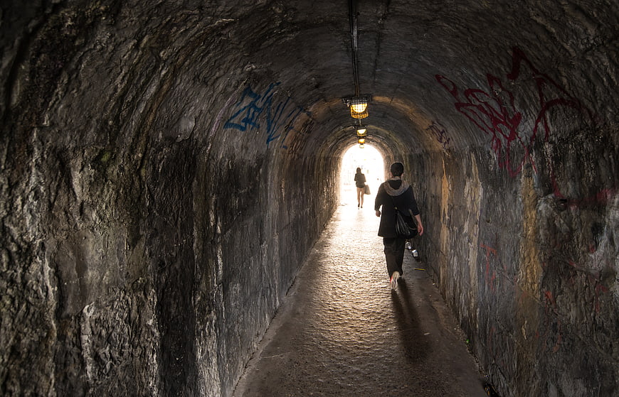 Woman walking through dark stone tunnel towards light