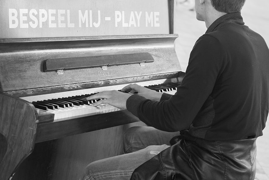 Man Playing Outdoor Piano with Play Me Sign