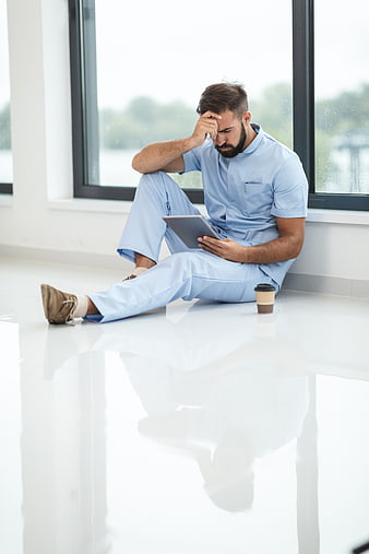 Stressed male nurse sitting on hospital floor with tablet
